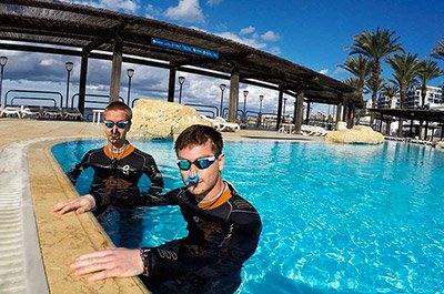 Two freedivers with nose clips an swimming googles on the edge of an outdoor pool