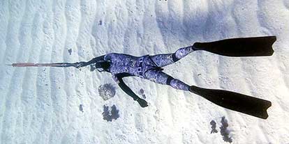 a spearfisher in Malta in a camouflage wetsuit on a sandy bottom