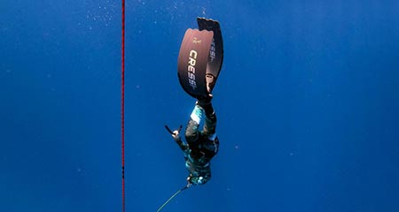 A female freediver with a camouflage wetsuit descending down the line in constant weight with her long freediving fins