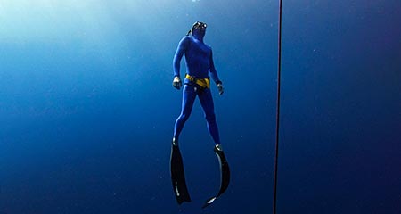 A male freediver in a blue wetsuit ascending 