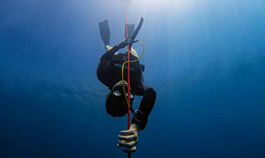 Advanced Freediver in Gozo in a black open cell wetsuit descending with the lanyard to the depths