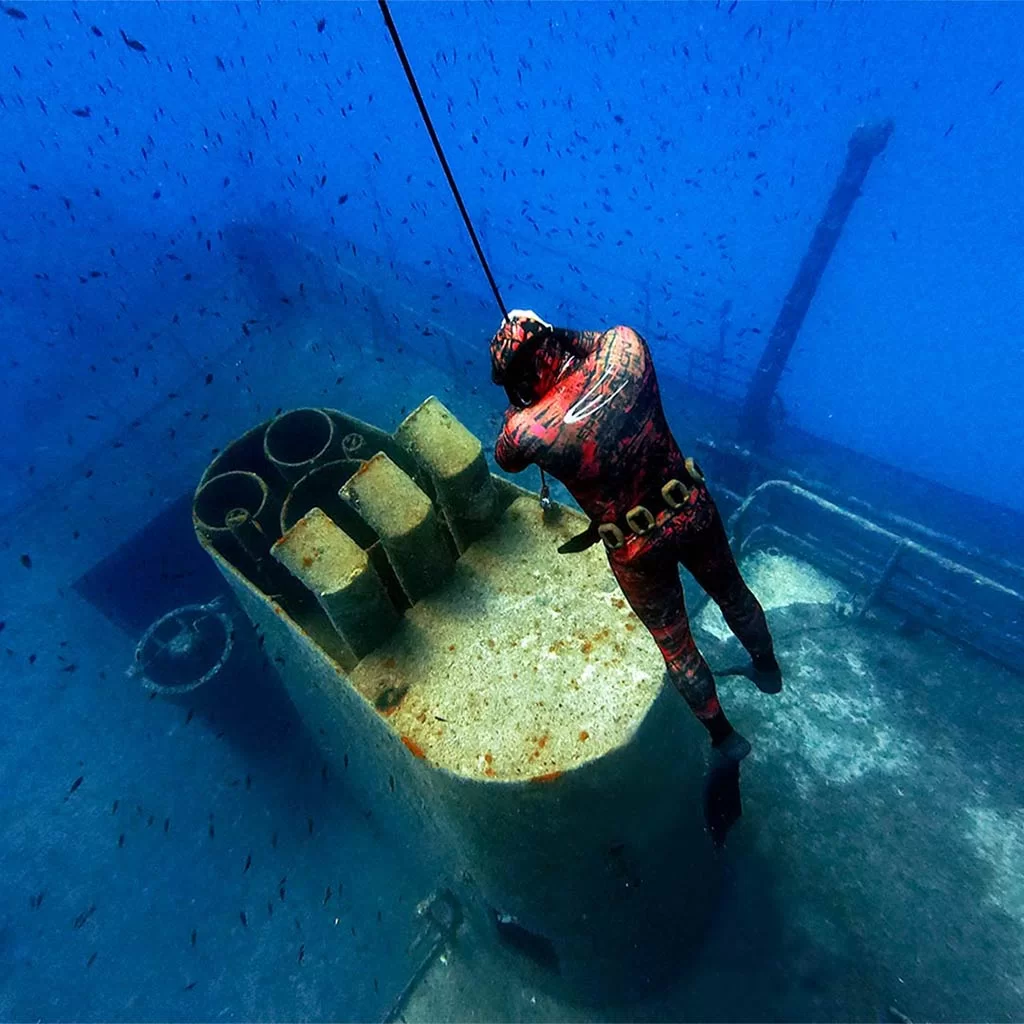 A freediver in Malta in a red freediving wetsuit holding the line on the top of a wreck